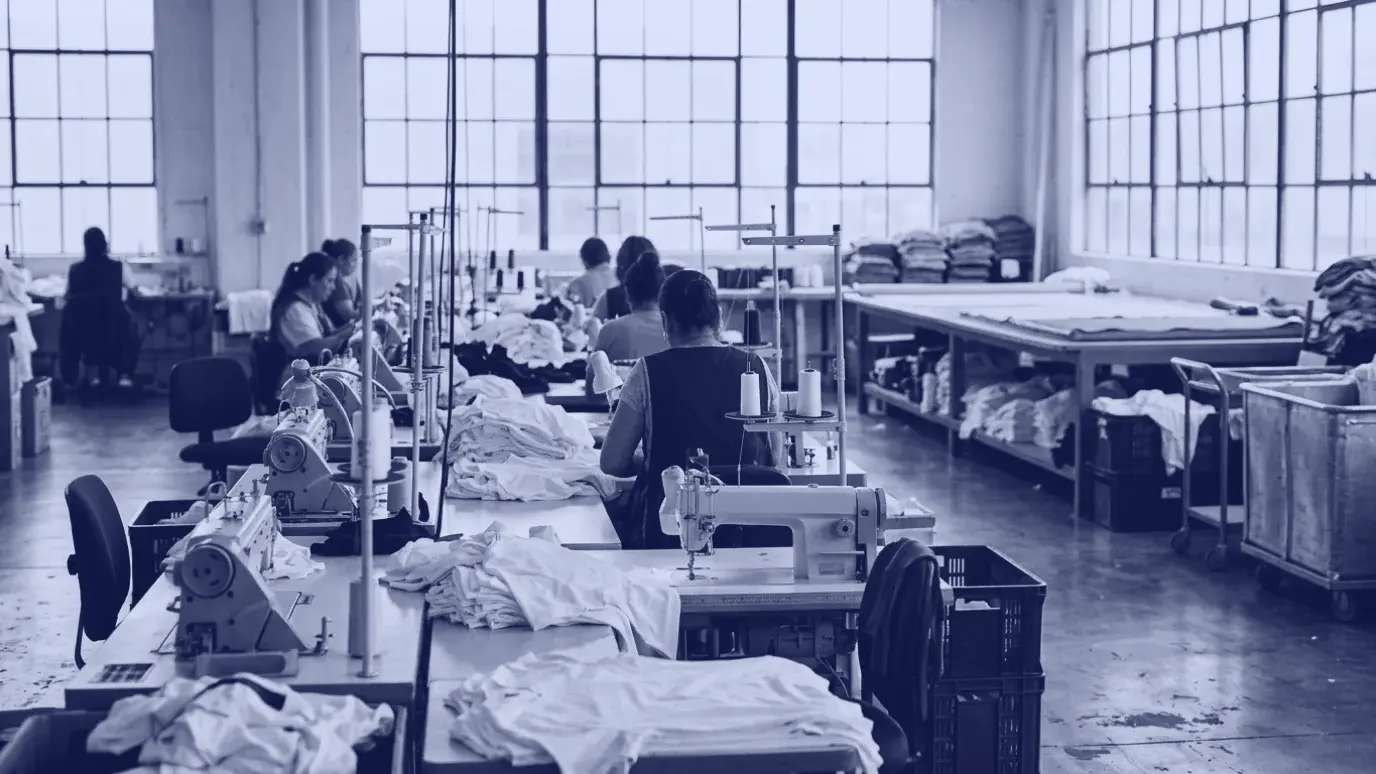 Row of industrial sewing machines and white t-shirt pieces in a bright garment production hall