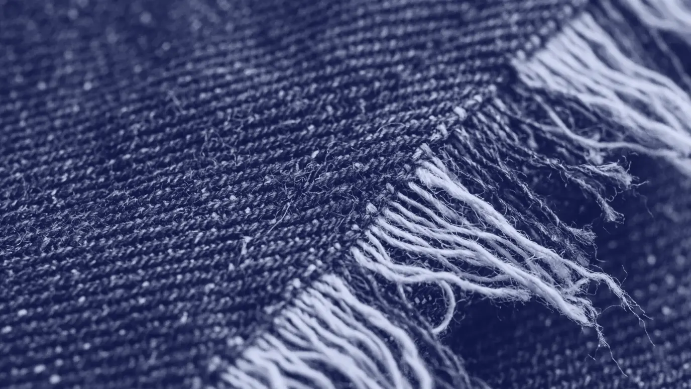 Ham indigo denim kumaşın yakın çekimi: diyagonal dimi çizgileri, saçaklı kenarda mavi çözgü ve beyaz atkı iplikleri
