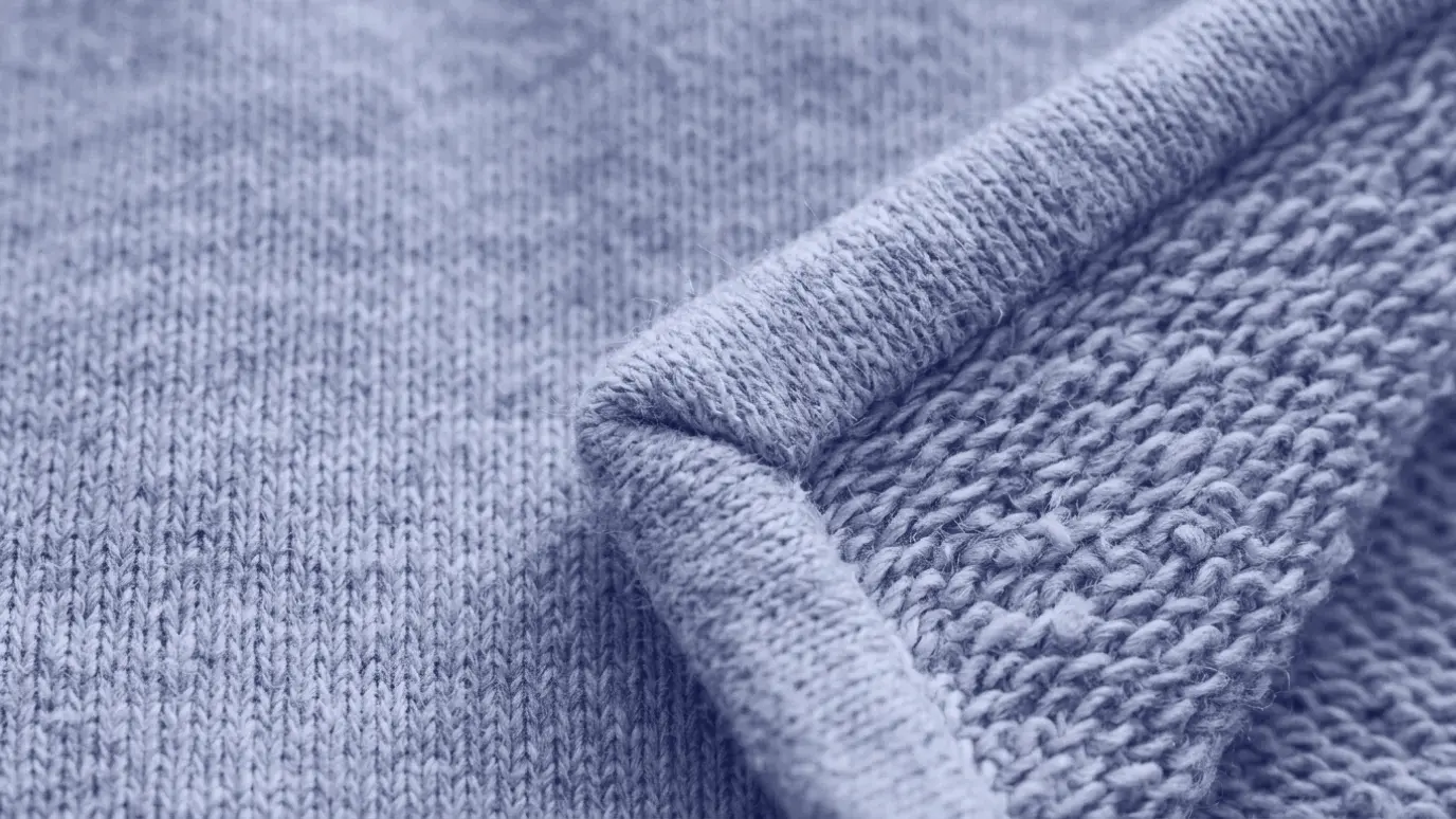 Macro of grey cotton two-thread fleece, a smooth front face and a lightly raised, fuzzy reverse at the folded corner