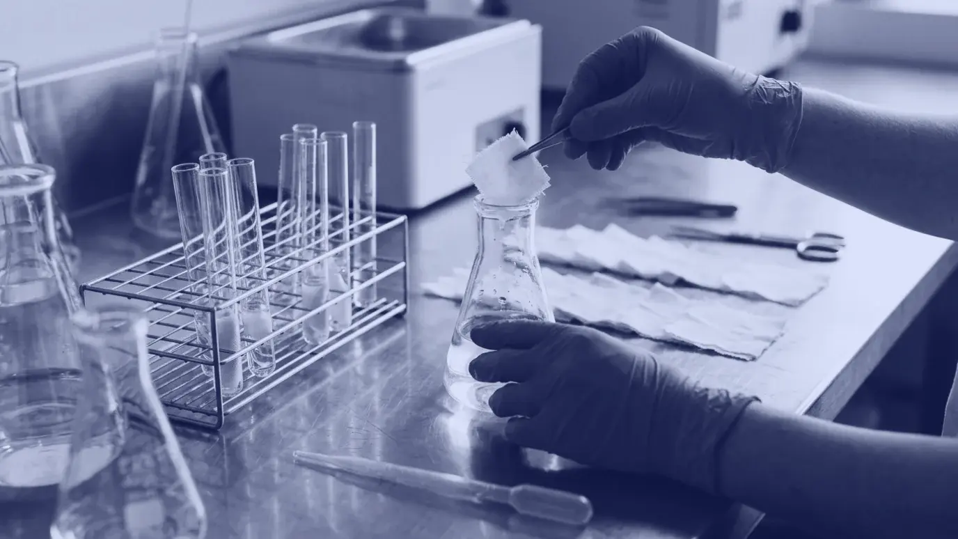 Tekstil test laboratuvarında eldivenli ellerle cam balona konan beyaz kumaş numunesi; yanda numune tüpleri
