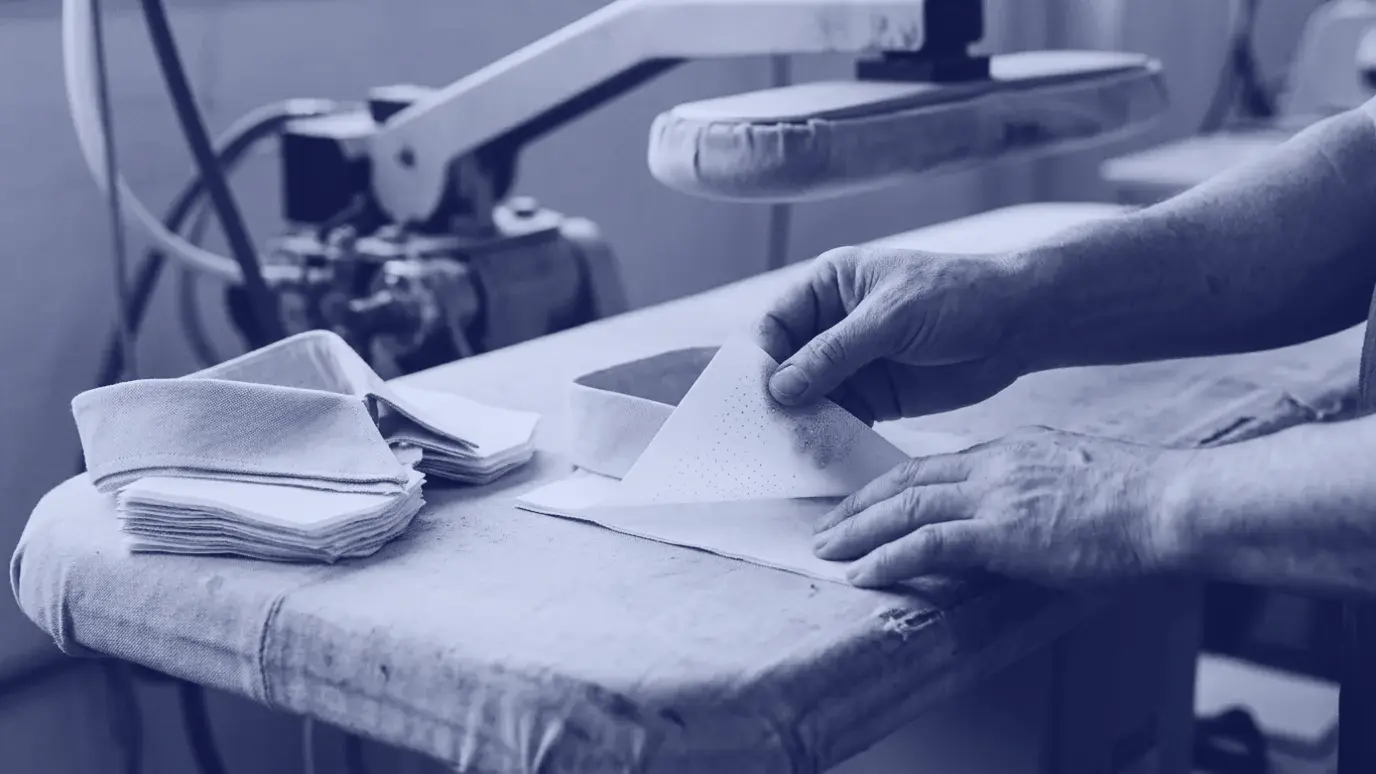 Hands laying fusible interfacing on a cut collar piece, a lifted corner showing the shiny adhesive dots