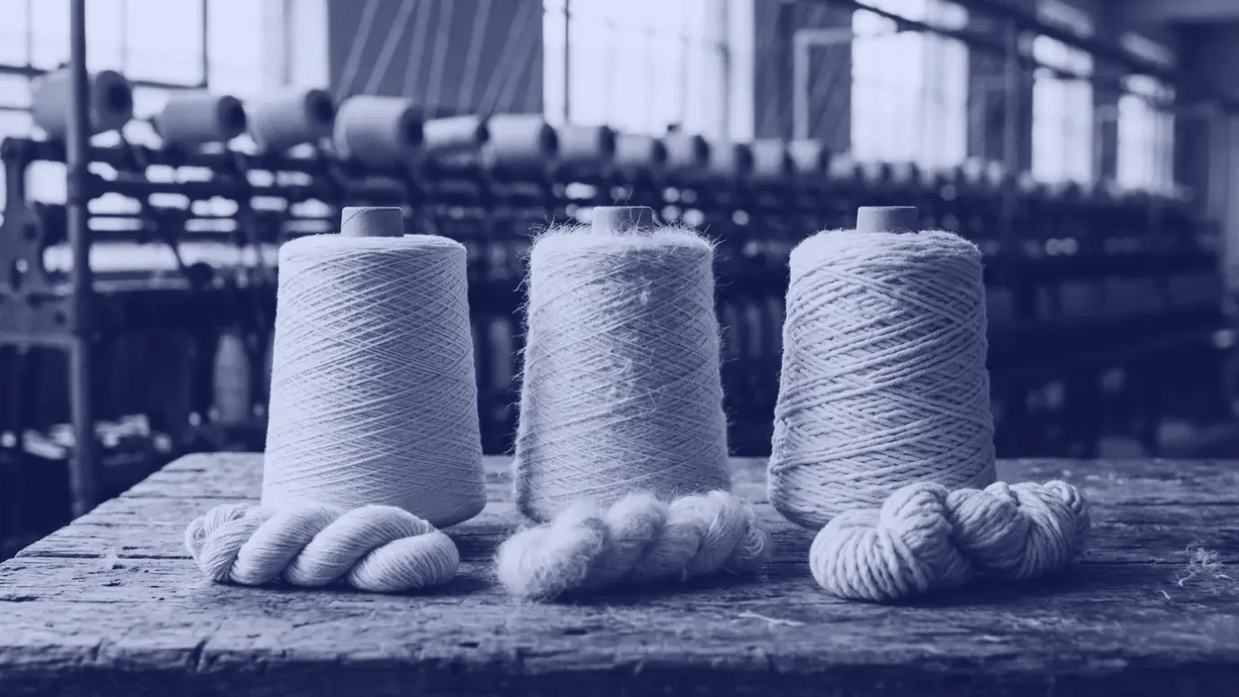 Three cotton yarn cones side by side on a wooden table with small hanks in front showing different yarn surfaces