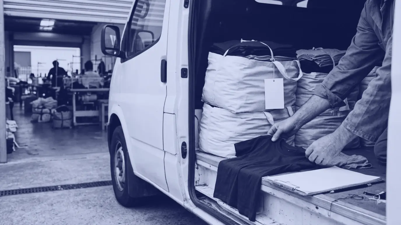 Atölye girişinde minibüsün açık kapısında, onaylı numune tişörtle atölyede dikilen ilk tişörtü karşılaştıran eller