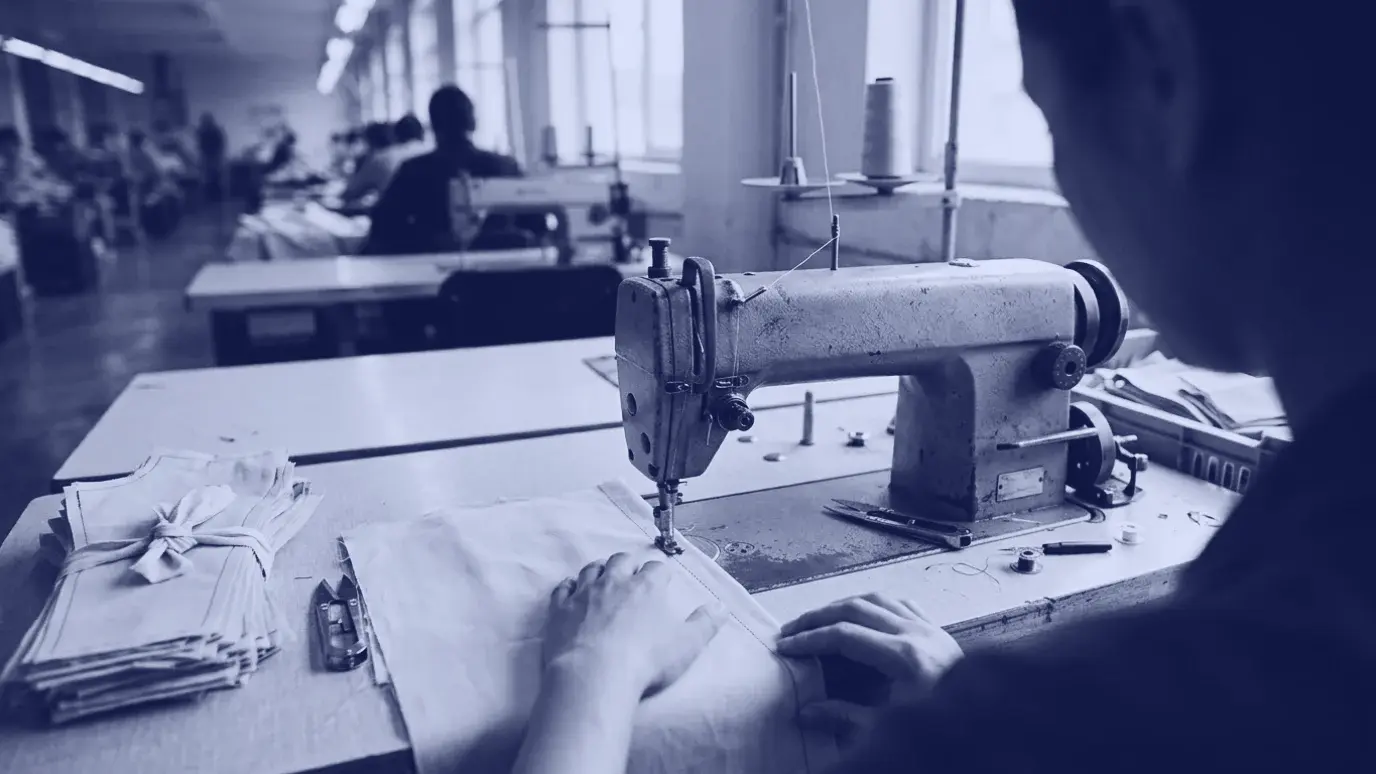 Düz dikiş makinesinde kumaş parçasını iğne altında yönlendiren eller; yanında kesilmiş parça desteleri ve iplik makaraları