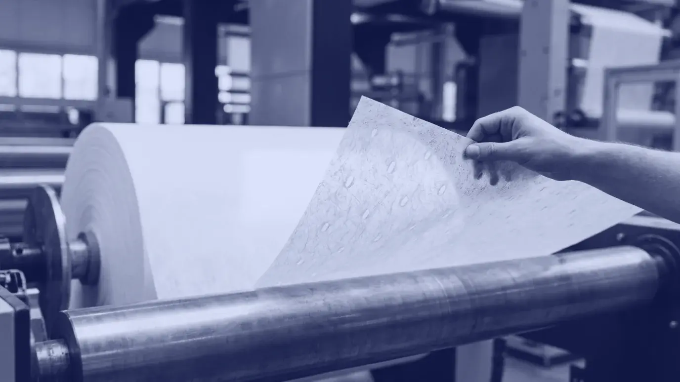 Silindirin üzerinden açılan beyaz spunbond nonwoven rulosu; ince tülbent yüzeyde düzenli bağlama noktaları, kenarı tutan el